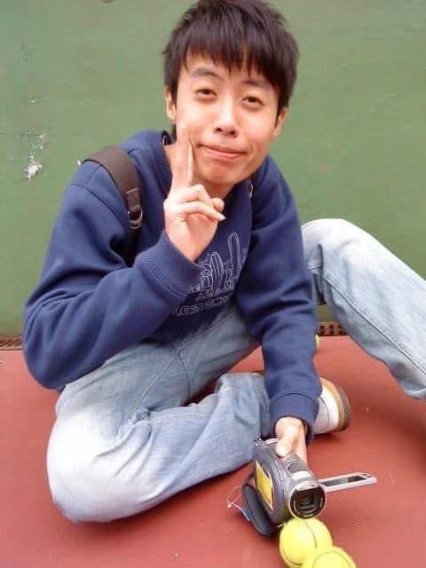 坐在球場地面上的年輕人，手邊放著手持攝影機與網球。