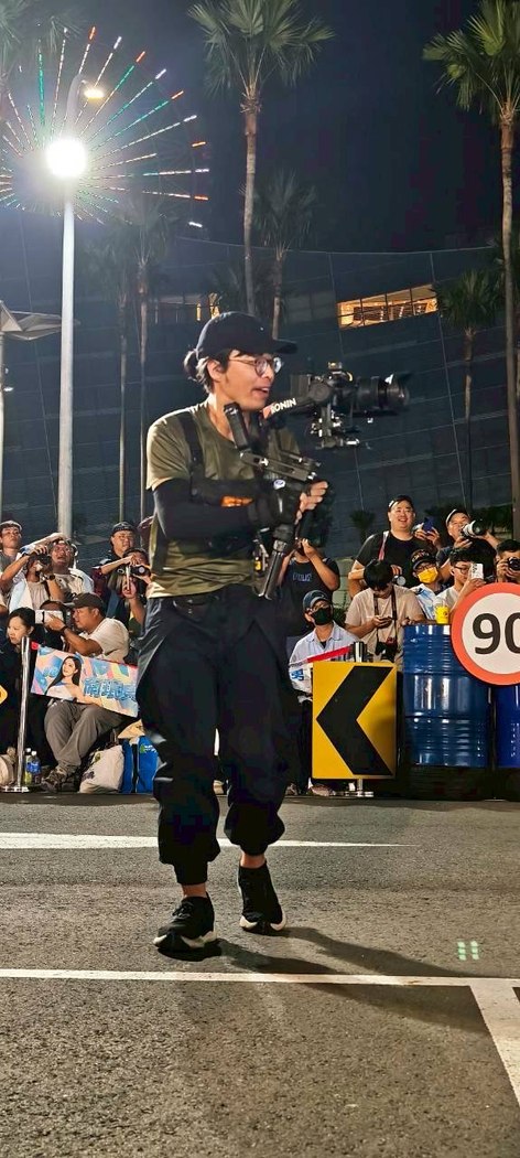 夜間活動中，攝影工作者手持穩定器，身後是參與者與燈光。